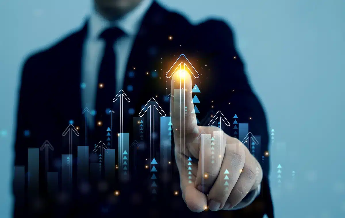 A person in a suit touches a glowing upward arrow symbol on a transparent screen, symbolizing growth and success in a business context.